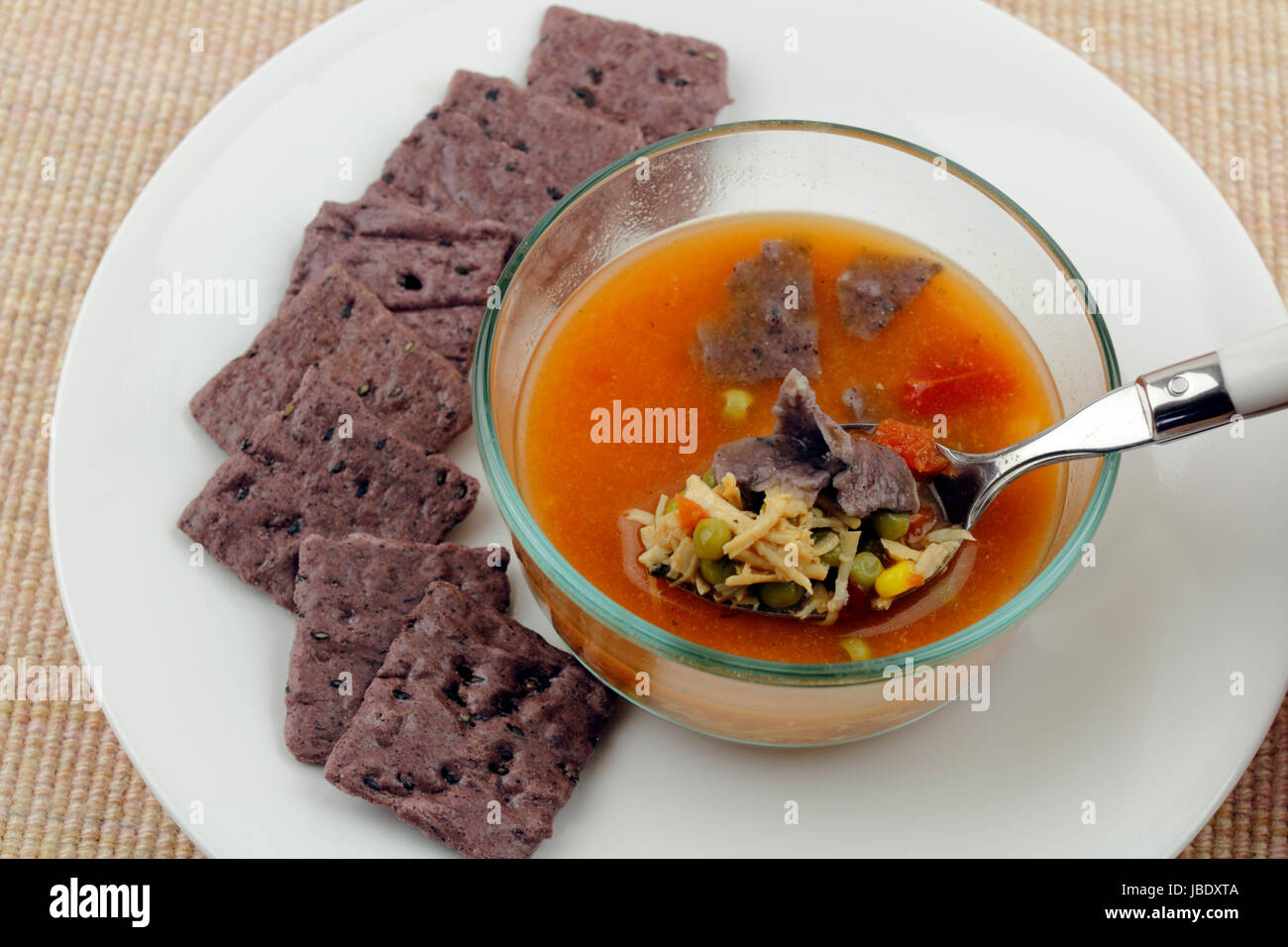 Spoon dipping into a glass bowl of homemade chicken soup consisting of shredded chicken, peas