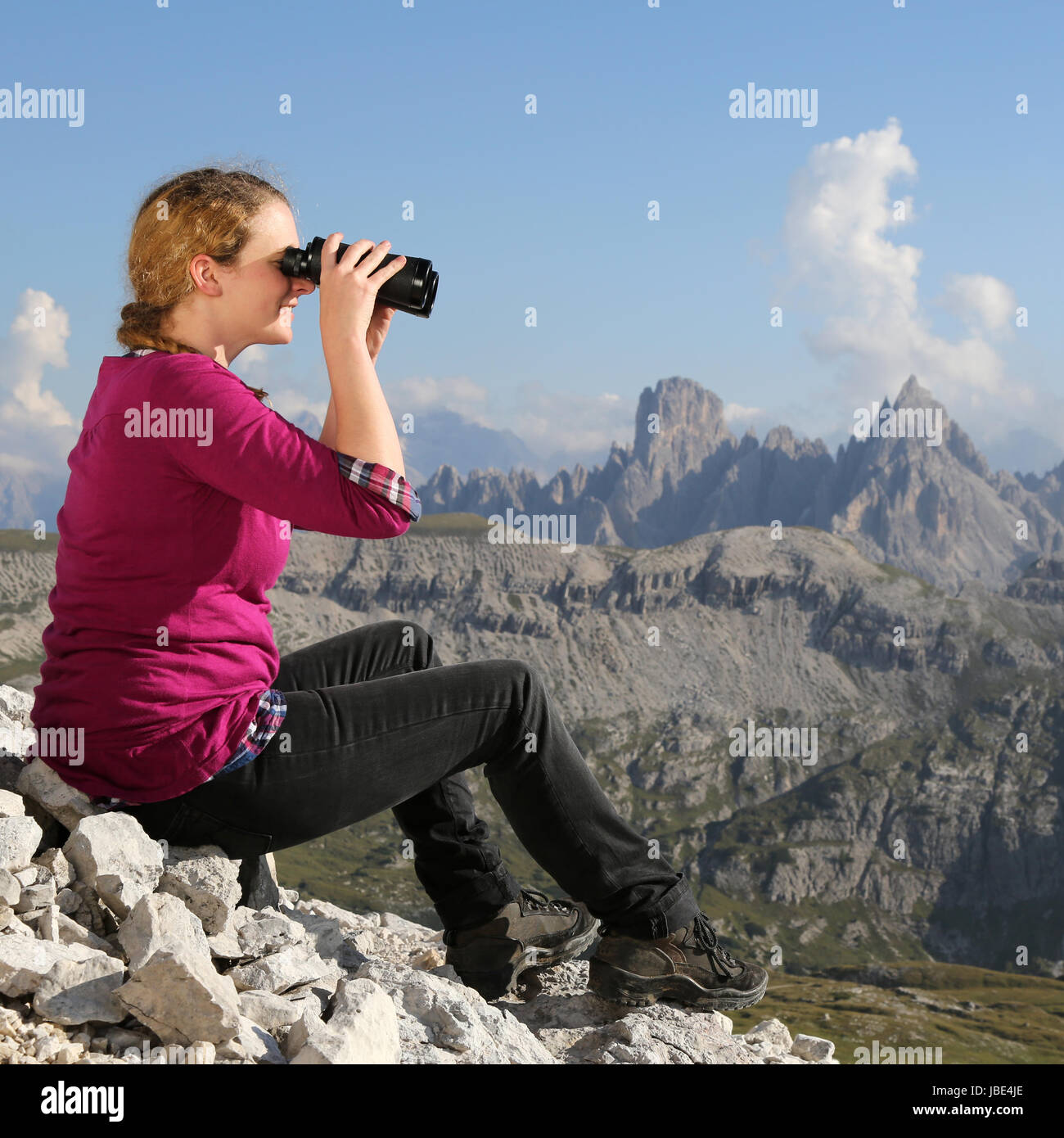 Eine junge Frau betrachtet die Landschaft in den Bergen durch ein Fernglas Stock Photo