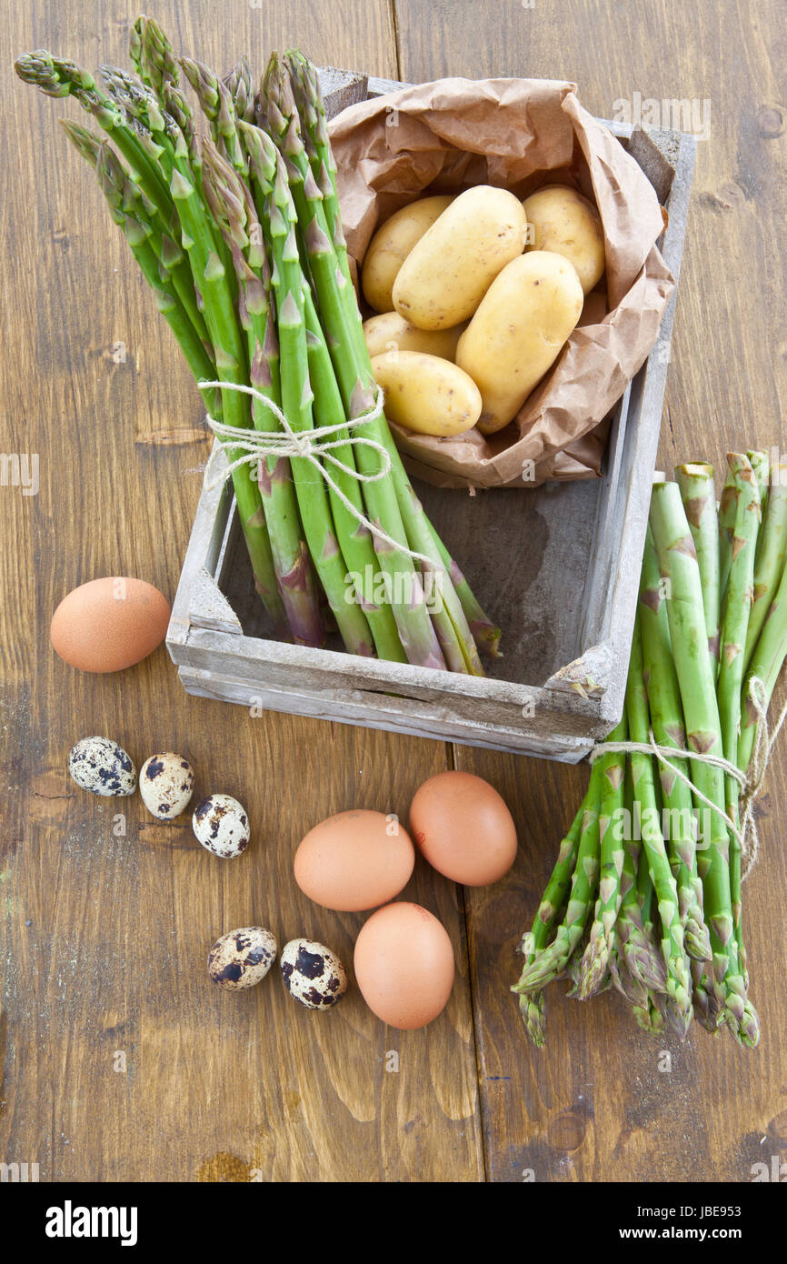 Frischer gruener Spargel , Bio-Kartoffeln und verschiedene rohe Eier in Holzkiste Stock Photo