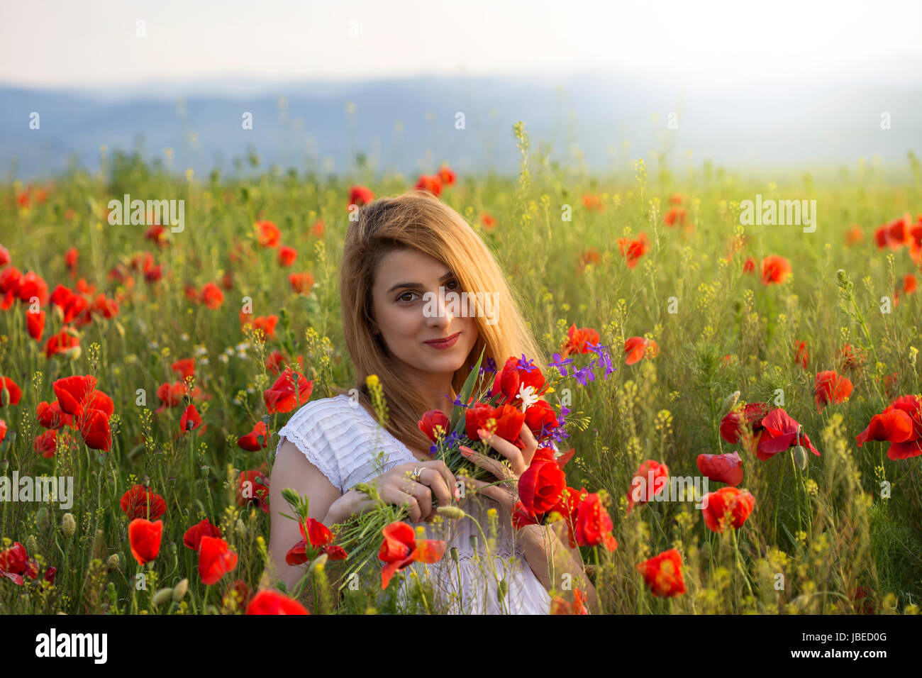 Beautiful happy woman in poppy field holding a bouquet of poppies Stock Photo