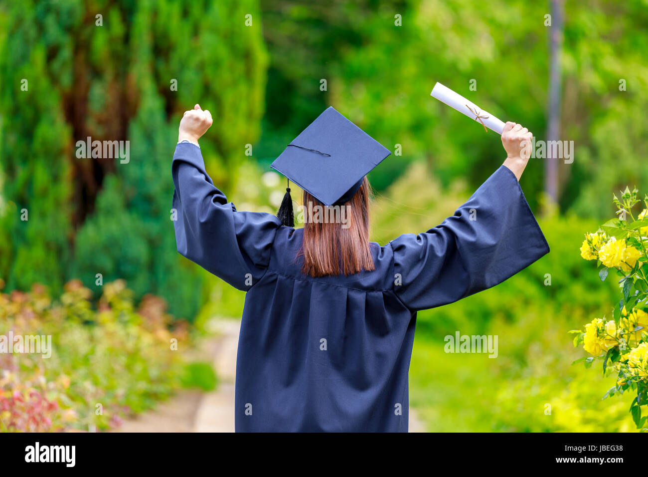 Young woman graduate put her hands up and celebrating with certificate in her hands and feeling so happiness in. Stock Photo