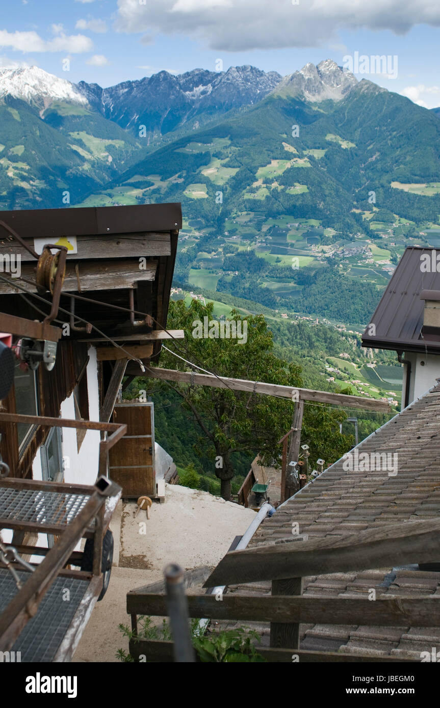 Blick von oberhalb der Bergstation Hochmuth (Dorf Tirol / Südtirol) zwischen die Dächer hindurch in Richtung der Berggruppe Iffinger auf der anderen Seite des Meraner Tals im Sommer Stock Photo