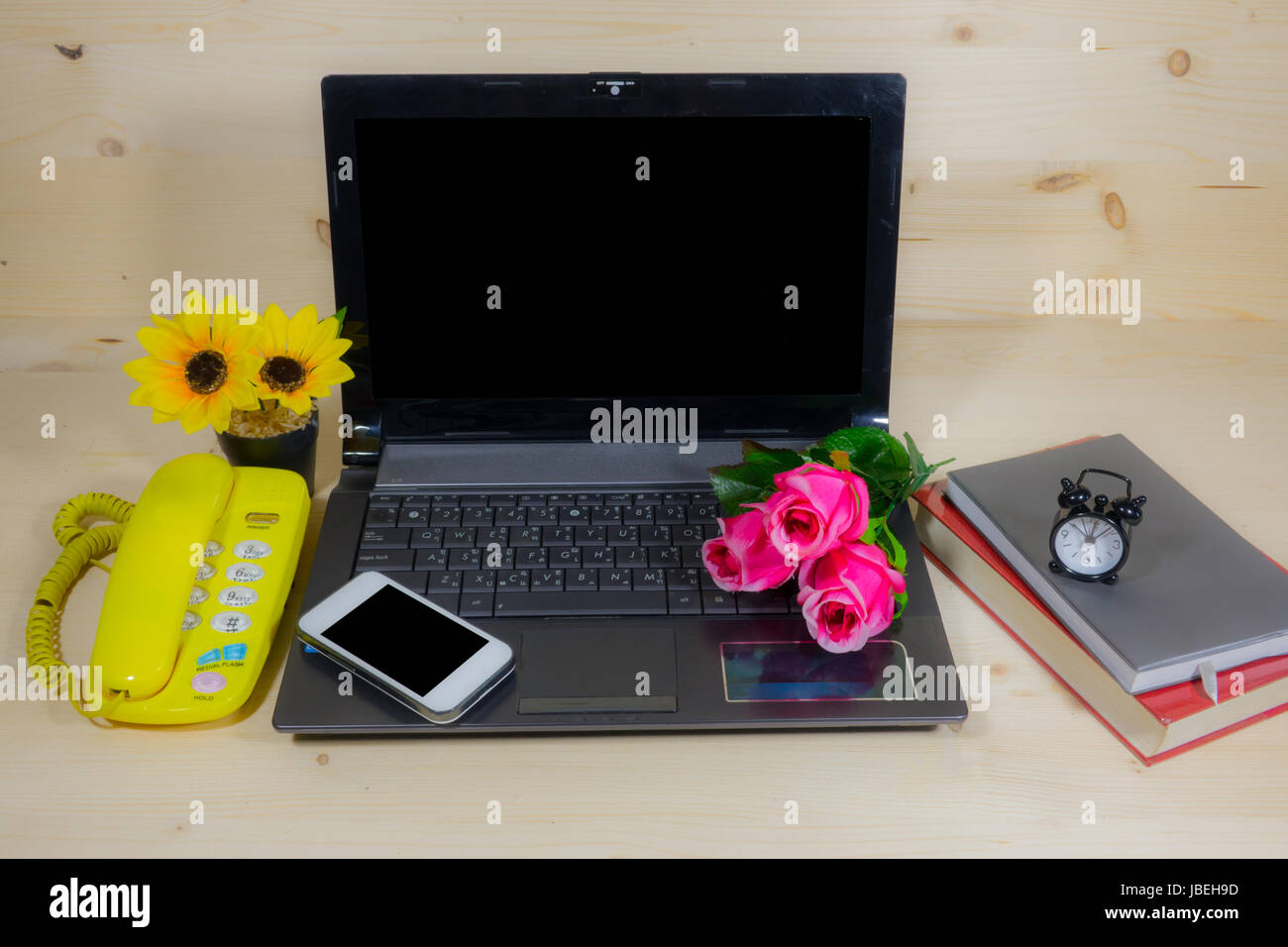 Working desk with many flowers on the laptop, phone, clock Stock Photo