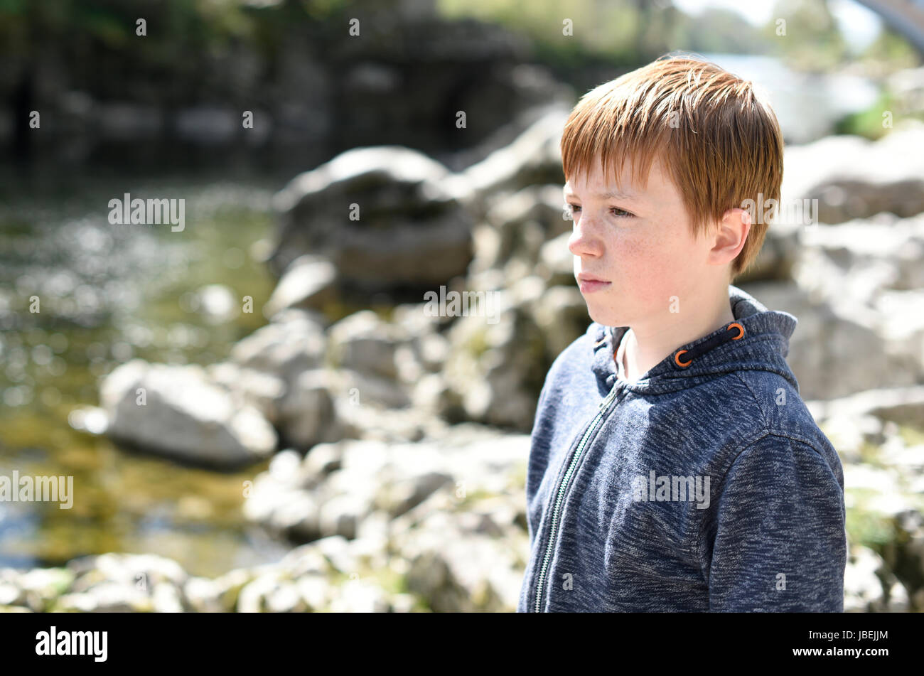 Young boy, looking out over the water from the riverside in Kirkby Lonsdale, Cumbria Stock Photo