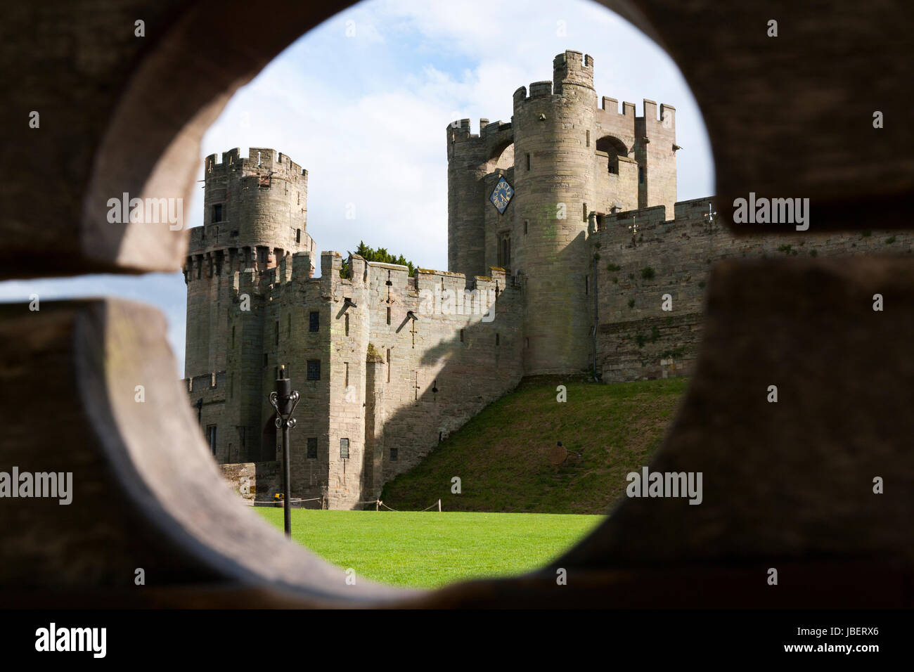 Barbican battlements, front, with the taller Gatehouse / Gate House in the background, seen through wooden stocks. Warwick castle in Warwickshire, UK Stock Photo
