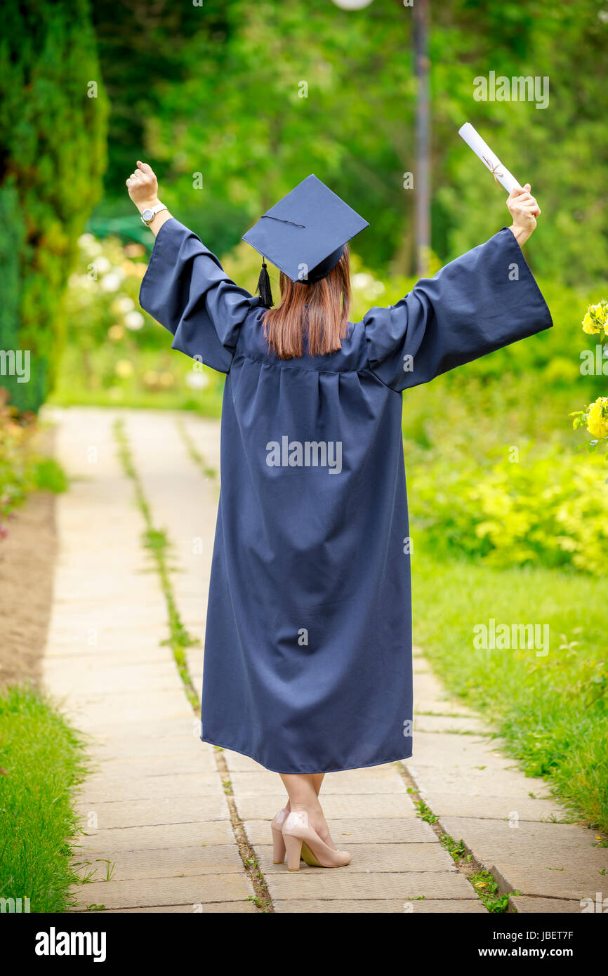 Young woman graduate put her hands up and celebrating with certificate in her hand and feeling so happiness in Stock Photo