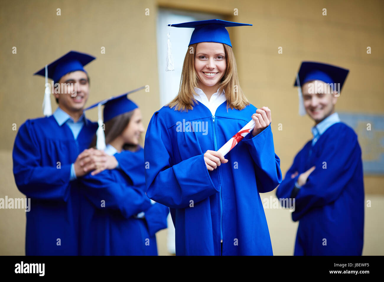 Friendly students in graduation gowns looking at camera with happy girl in front Stock Photo