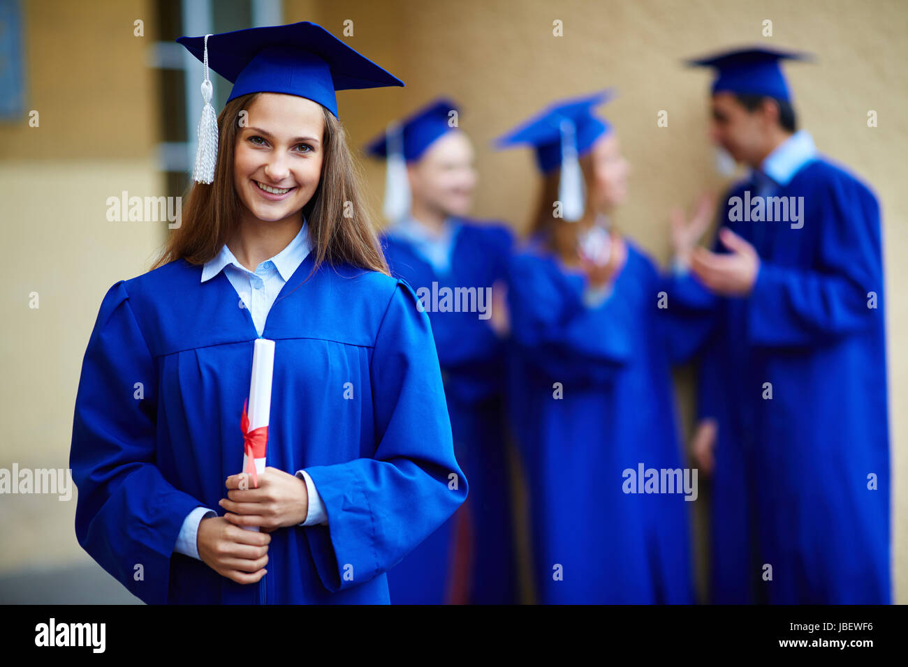 Friendly students in graduation gowns talking with happy girl in front Stock Photo