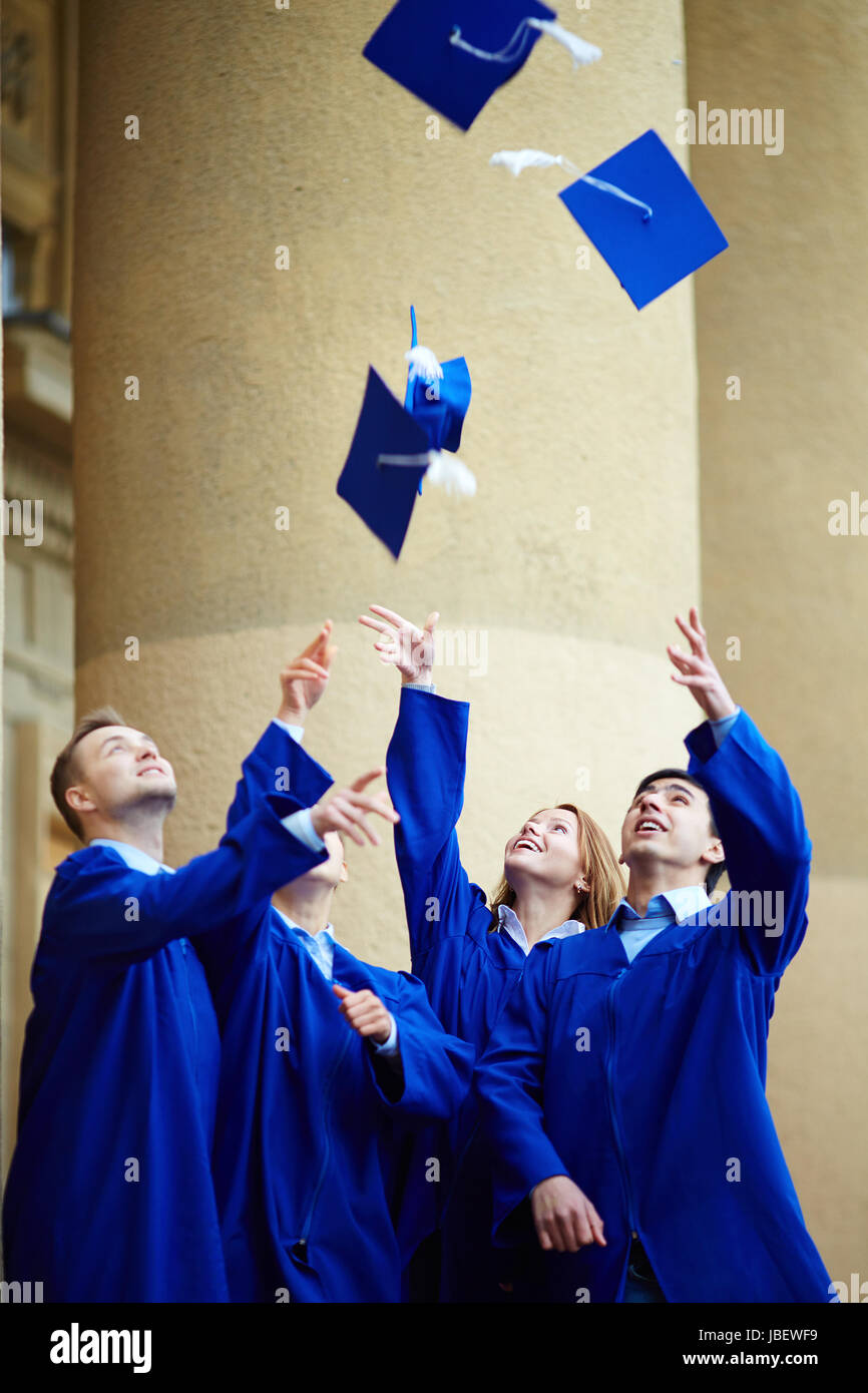 Group of smart students in graduation gowns throwing their hats Stock Photo