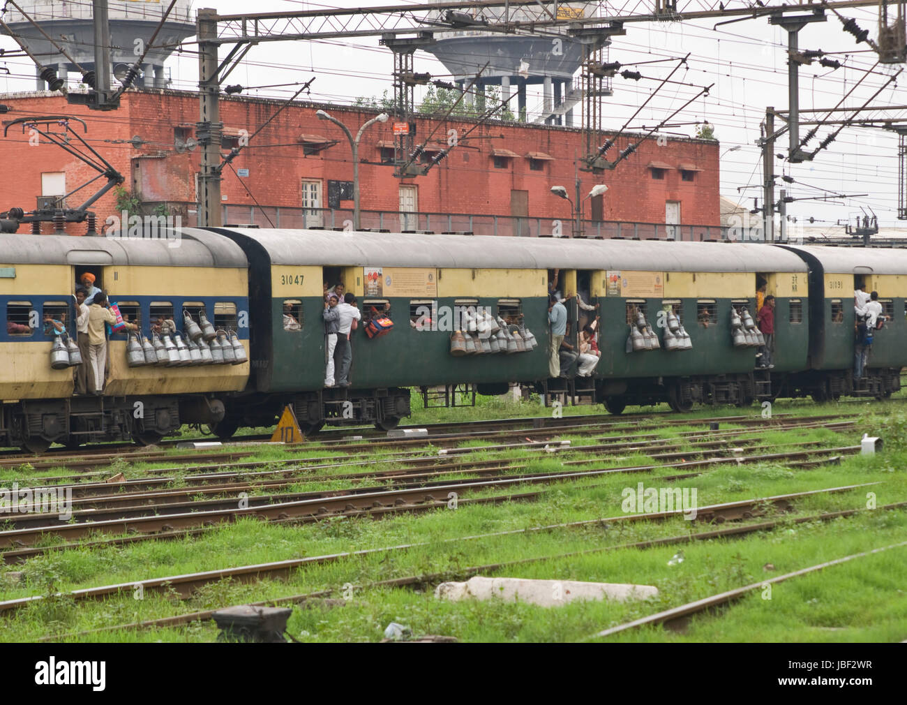 People hanging onto the doorway of a moving train. Milk churns attached to the windows. Old Delhi, India. Stock Photo