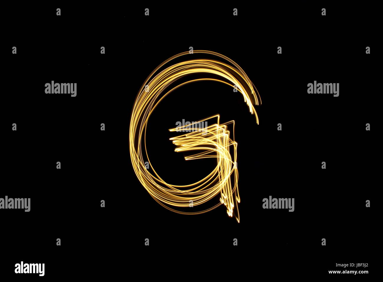 Gold letter G, Light Painting Photography, alphabet series, against a black background Stock Photo