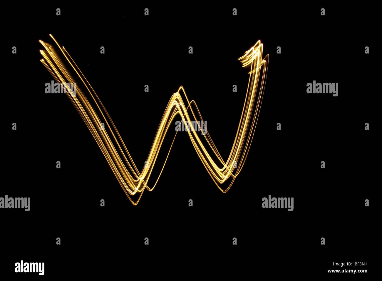 Gold letter W, Light Painting Photography, alphabet series, against a black background Stock Photo