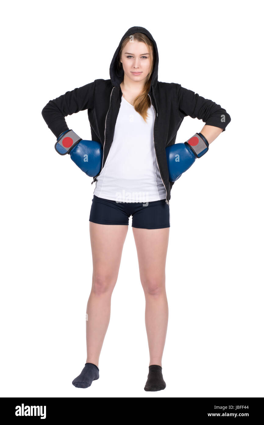 Freigestelltes Foto einer jungen böse schauenden Boxerin im Kapuzenpulli und mit blauen Boxhandschuhen, die sie in ihre Hüften stemmt Stock Photo