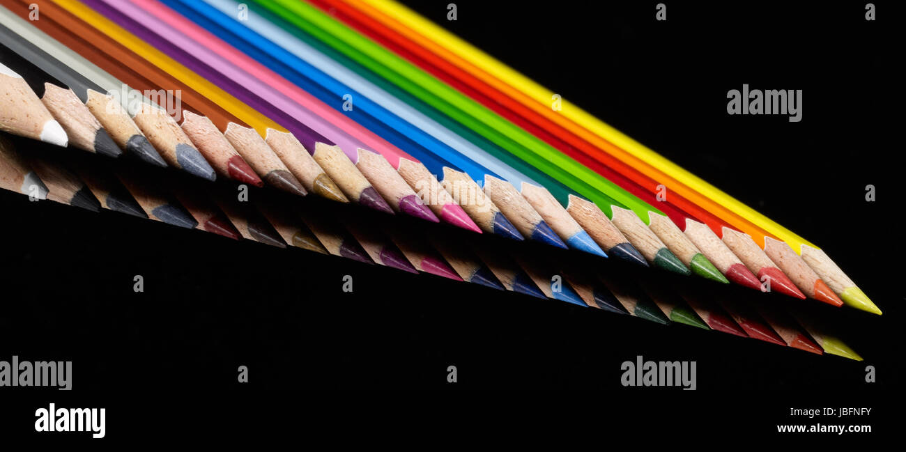 lots of colorful pencils in a row on black reflective back Stock Photo