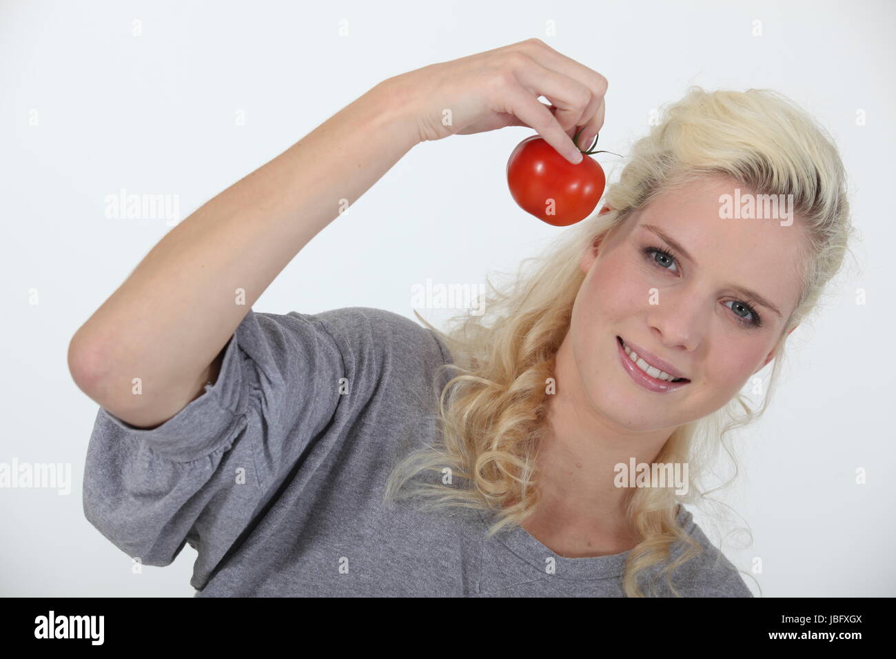 Smiling blond woman holding tomato on white background Stock Photo - Alamy