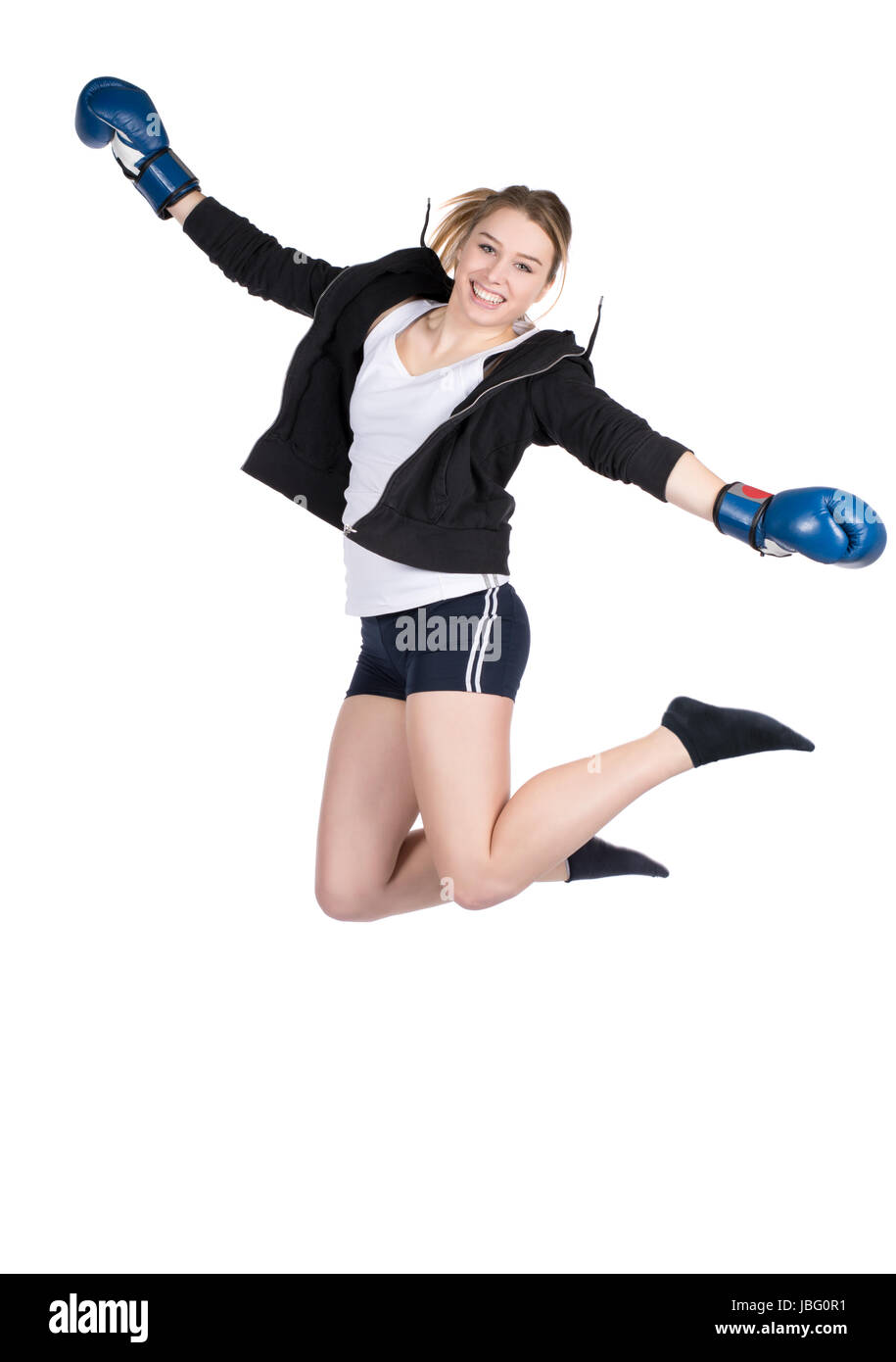 Freigestelltes Foto einer jungen lächelden Boxerin im Kapuzenpulli und mit blauen Boxhandschuhen, die in die Luft springt Stock Photo