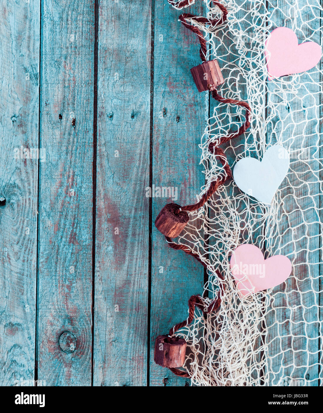 Border of romantic pink and white hearts in fishing net with an edge  decoration of corks in vertical format on rustic turquoise blue boards with  copyspace for your Valentine or anniversary greeting