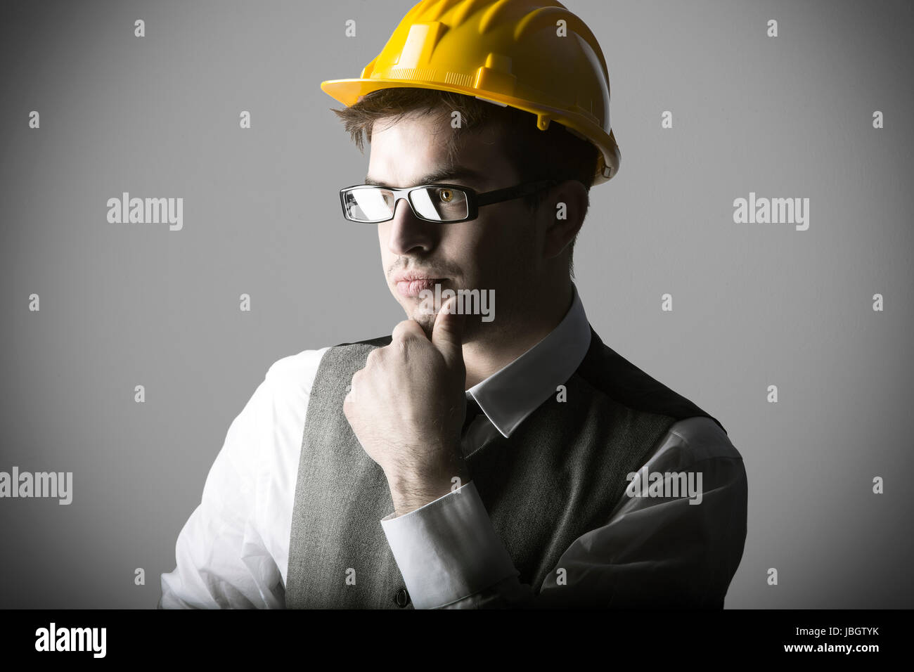 Portrait of thoughtful smart young engineer with helmet against grey background Stock Photo