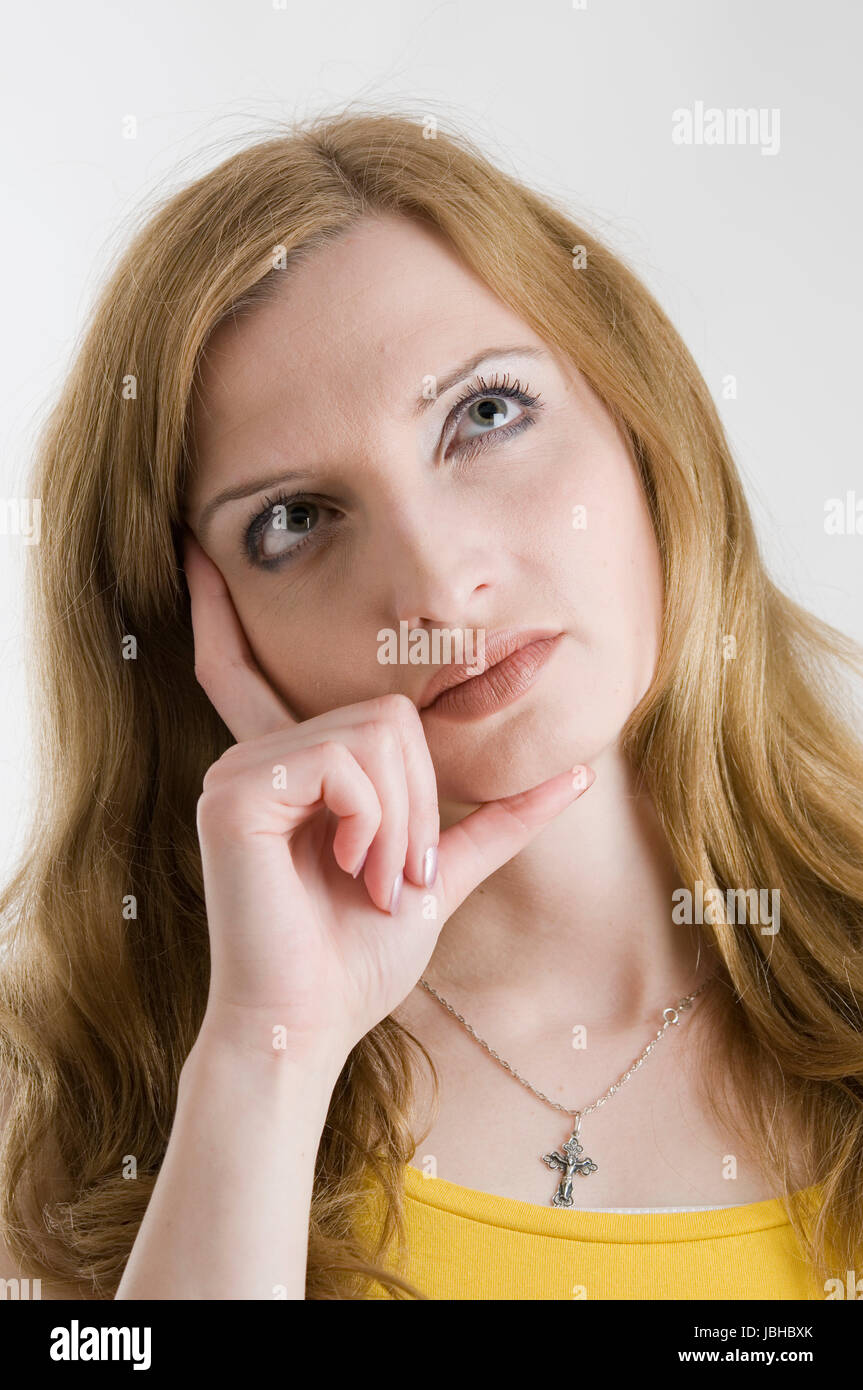 Kopf-und-Schulter-Porträt einer jungen blonden Frau nachdenklich nach oben blickend und sich auf die rechten Finger abstützend Stock Photo