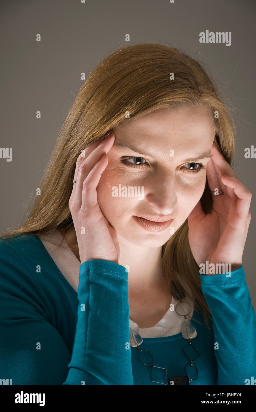 Kopf-und-Schulter-Porträt einer jungen blonden Frau mit gesenkten Blick und sich die Finger an die Schläfen haltend im Unterlicht Stock Photo