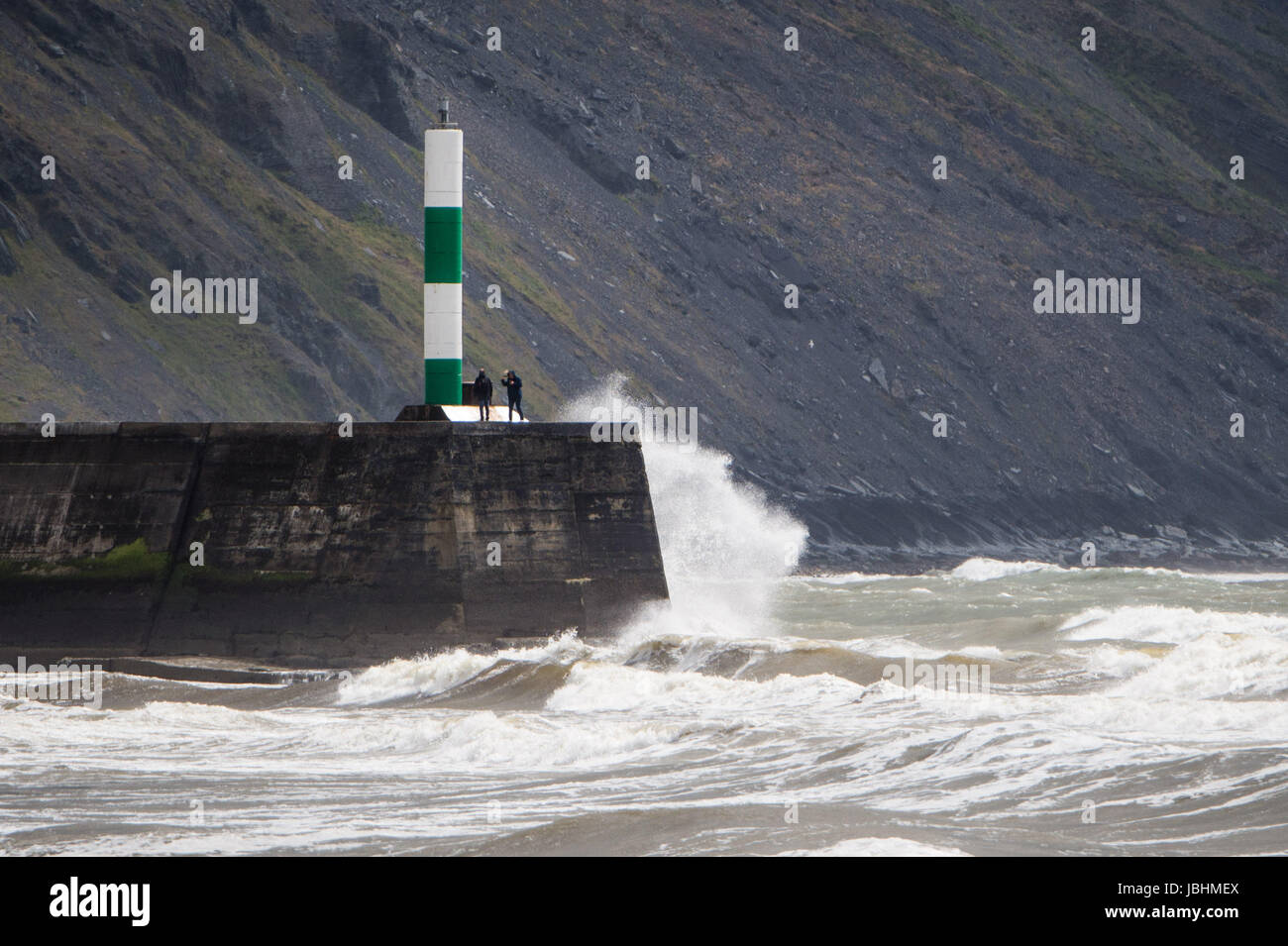 Aberystwyth Wales UK, Sunday 11 June 2017  UK Weather: Two people standing on the harbour wall as waves crash around them on a blustery summer sunday afternoon in Aberystwyth  on the Cardigan Bay coast of west  Wales  Photo credit: Keith Morris / ALAMY Live News Stock Photo