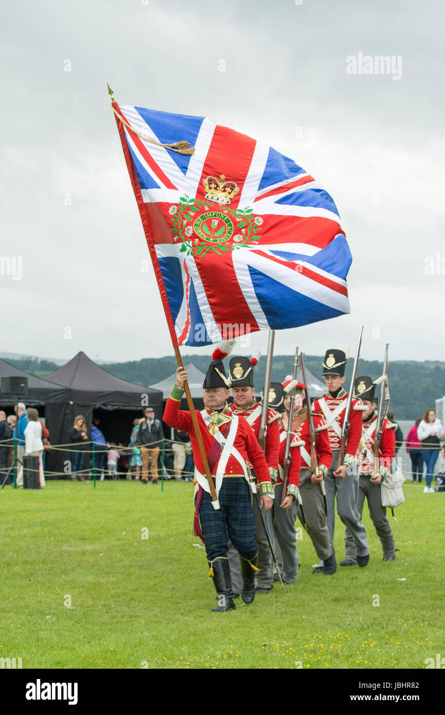Dumbarton, West Dunbartonshire, Scotland, UK - 11 June 2017: UK weather - a Napoleonic soldier controlling a very large flag during the two day Rock of Ages costume celebration of Scotland's history through the ages at Dumbarton Castle on a day of sunshine, gusty winds and showers Stock Photo