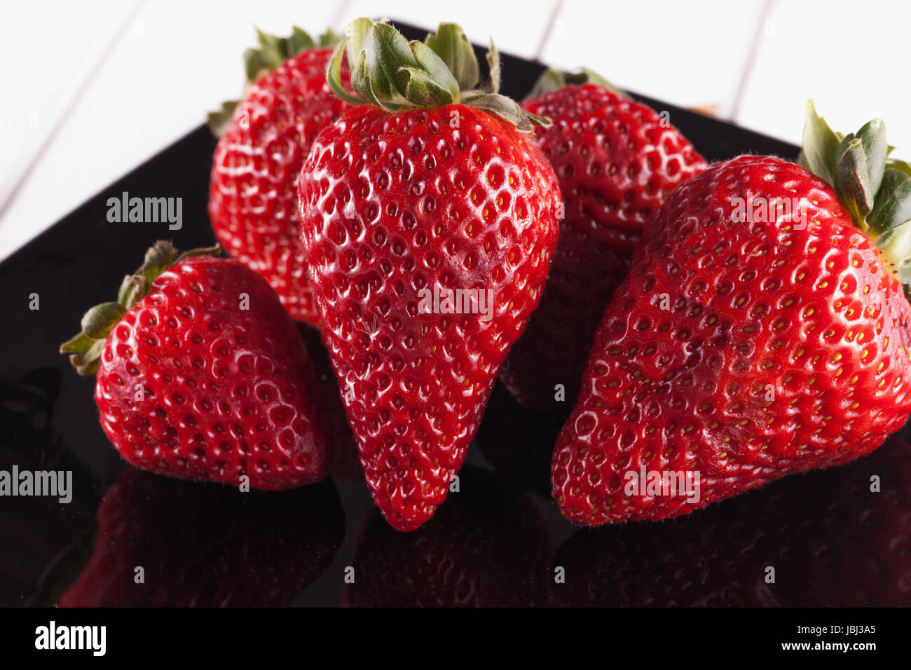 Strawberries over black plate, over white wood Stock Photo - Alamy