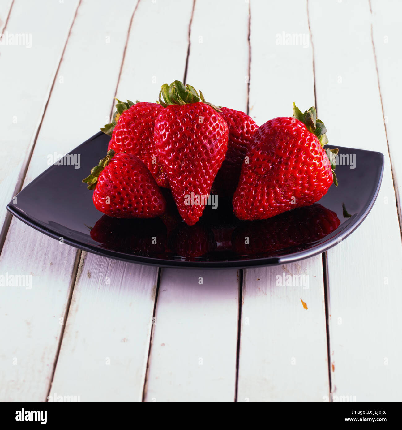 Strawberries over a black plate, over white wood Stock Photo - Alamy