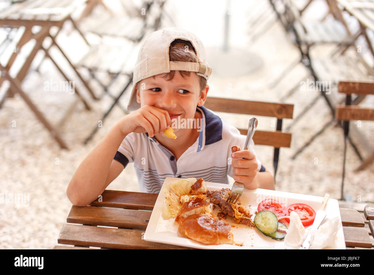 Little caucasian boy in cap eating street food in restaurant Stock Photo