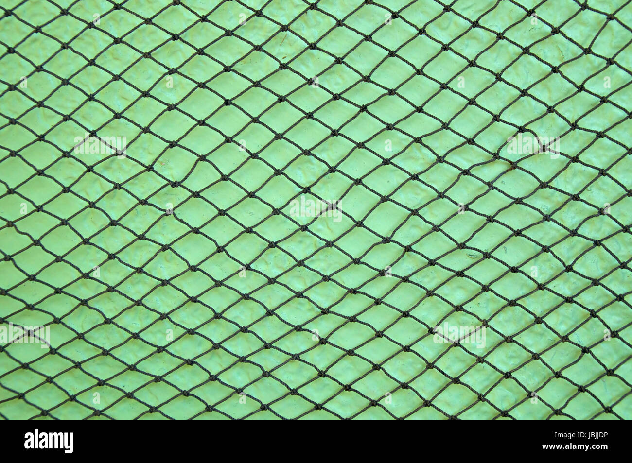 A knotted fishing net is stretched out hanging on a lime green stuccoed