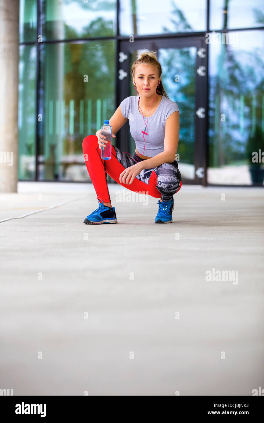 Sporty Woman Holding Water Bottle While Crouching On Footpath Stock Photo