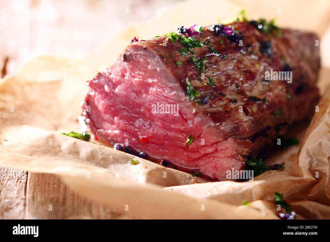 Tender lean rare roast beef seasoned with fresh herbs and spices on a piece of oven paper Stock