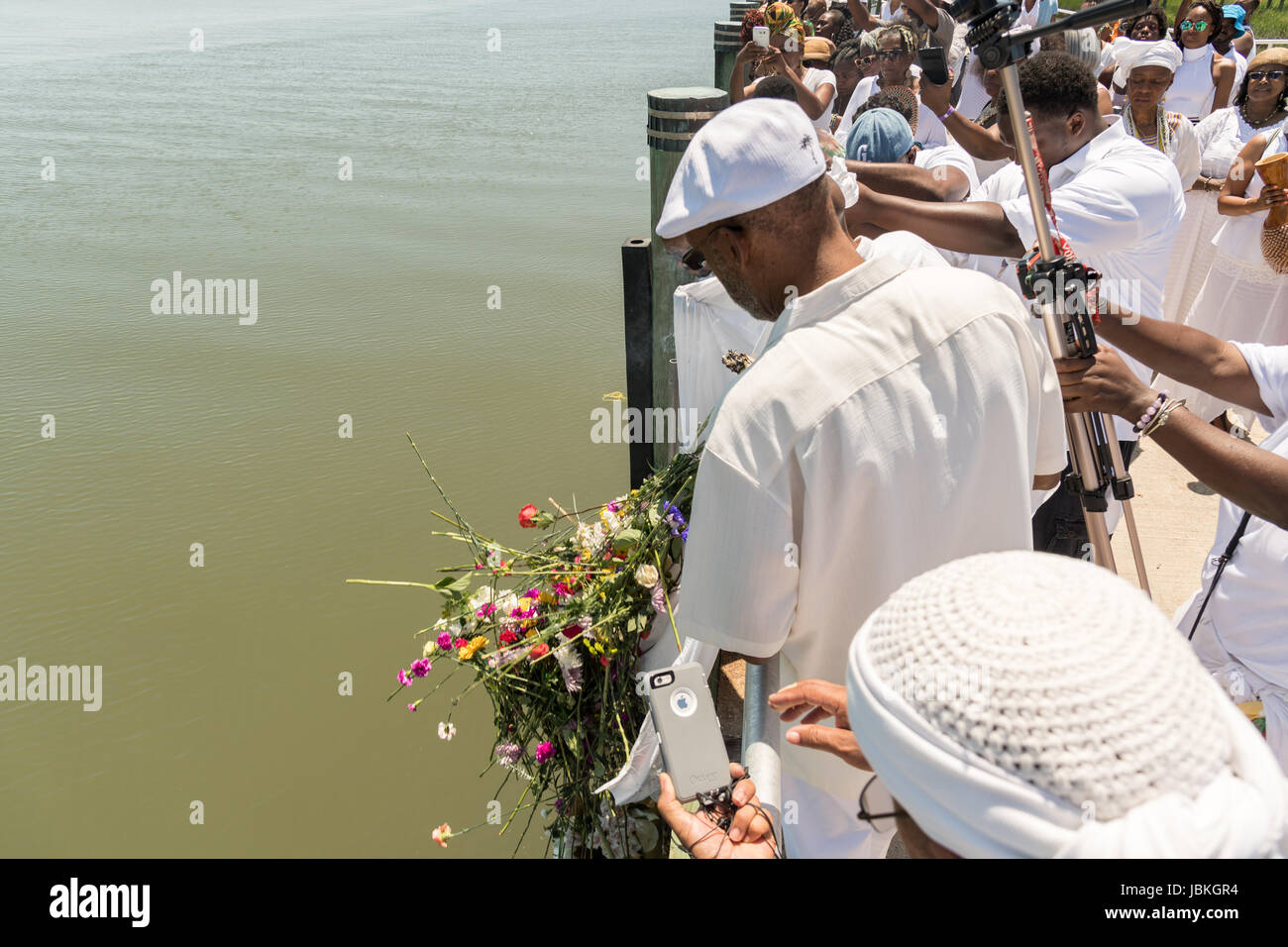 Public radio host of the Roots Musik Karamu show, Osei Chandler drops flower offerings in the water during a remembrance ceremony for enslaved Africans that died in the Middle Passage June 10, 2017 in Sullivan's Island, South Carolina. The Middle Passage refers to the triangular trade in which millions of Africans were shipped to the New World as part of the Atlantic slave trade. An estimated 15% of the Africans died at sea and considerably more in the process of capturing and transporting. The total number of African deaths attributable to the Middle Passage voyage is estimated at 2 million. Stock Photo