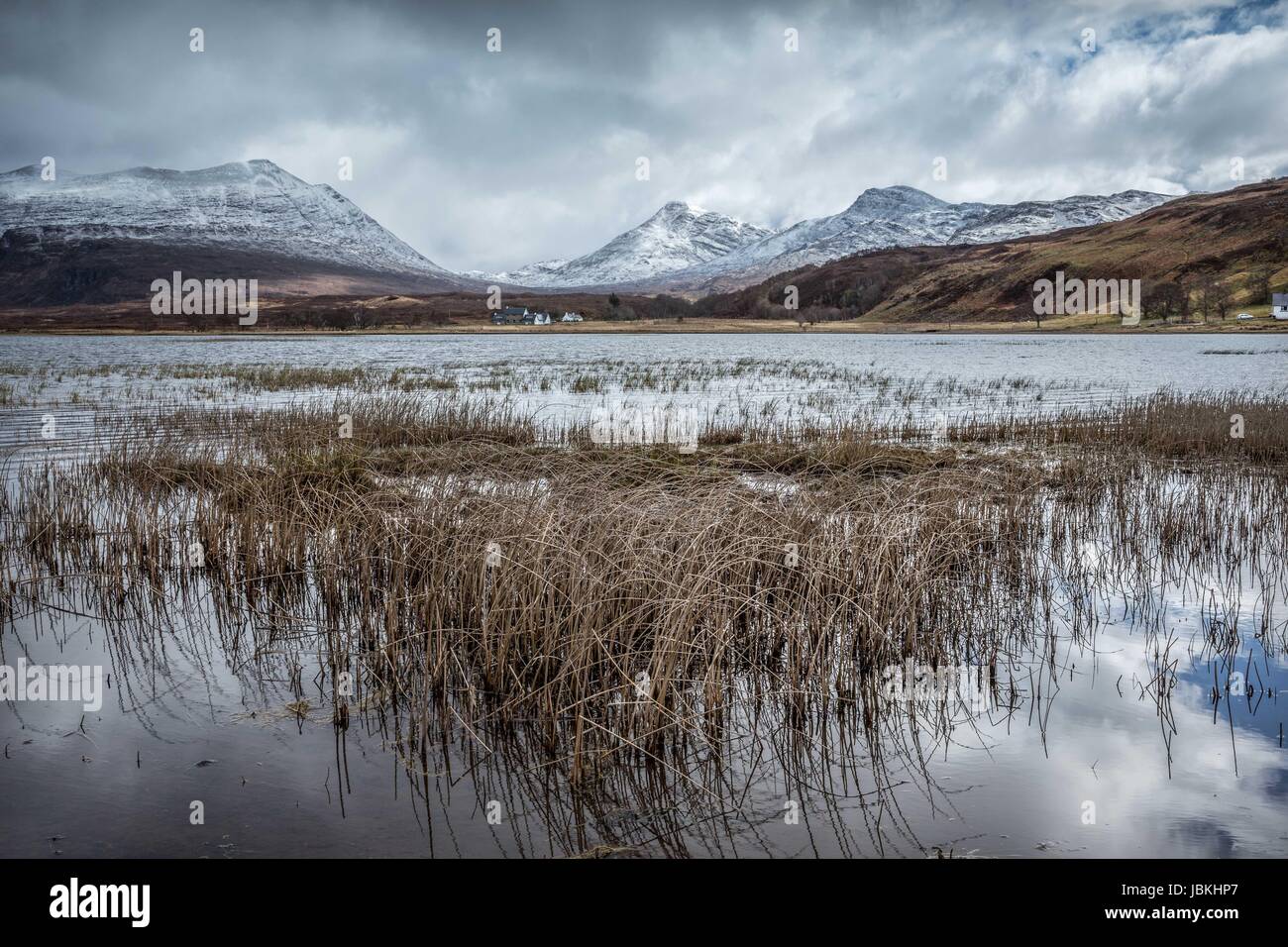 View of Loch Damh, Torridon, Scotland; with An Ruadh-stac and Sgurr a'Gharaidh in the distance; snow on mountains and rushes reflected in foreground Stock Photo