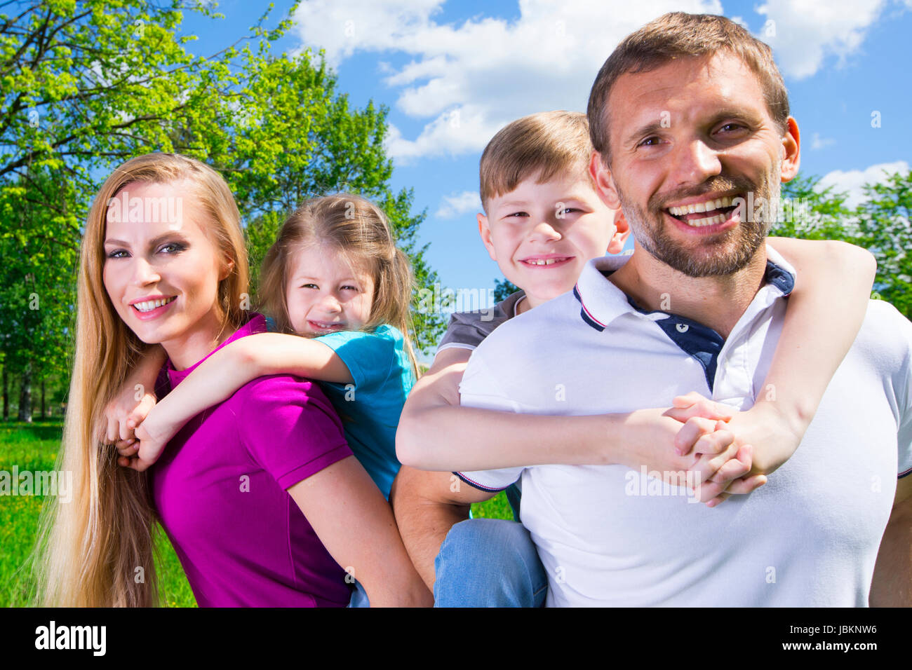 Happy family portrat, couple giving two young children piggyback rides ...