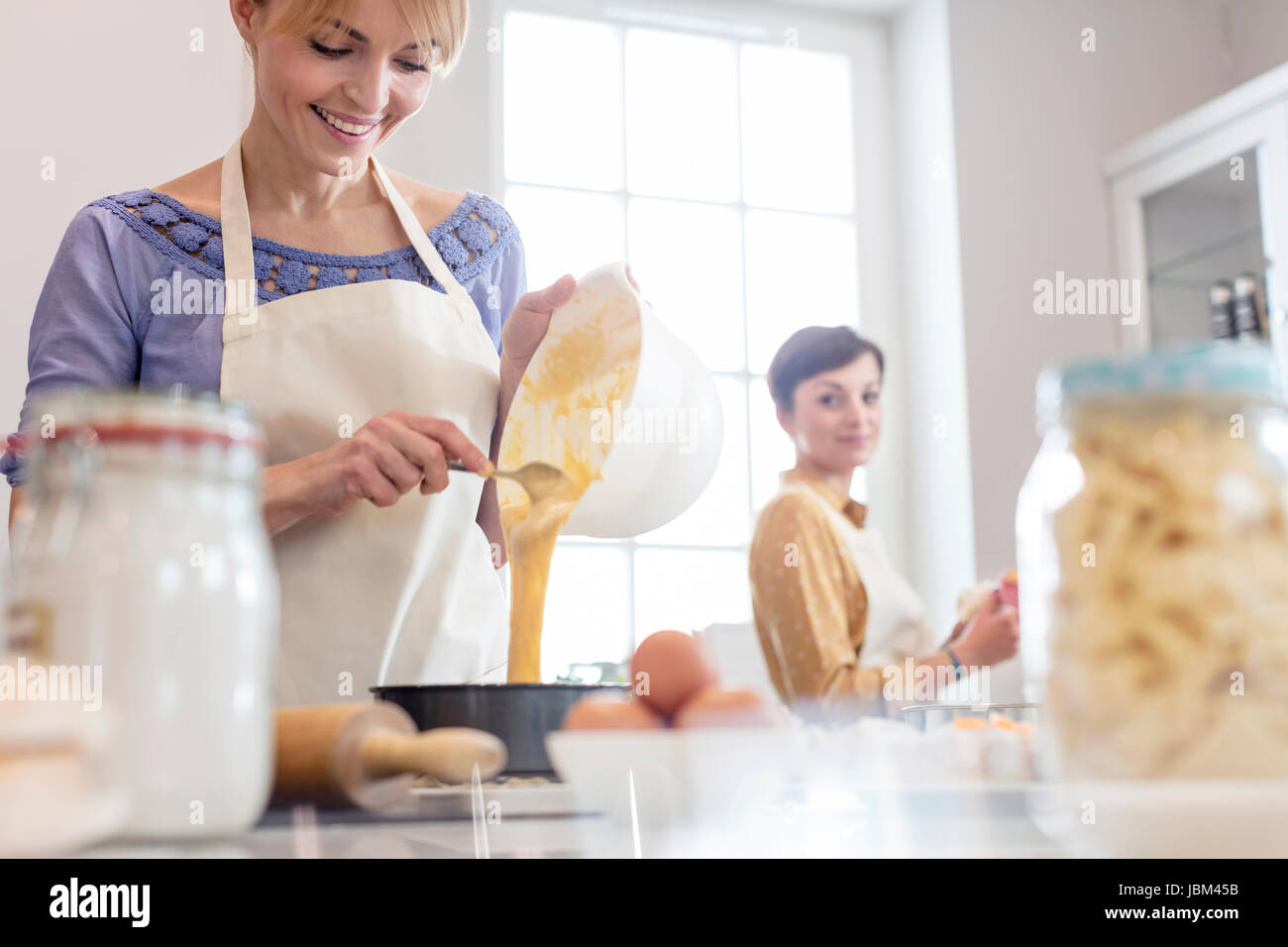 Female caterers baking, pouring cake batter into tin in kitchen Stock Photo
