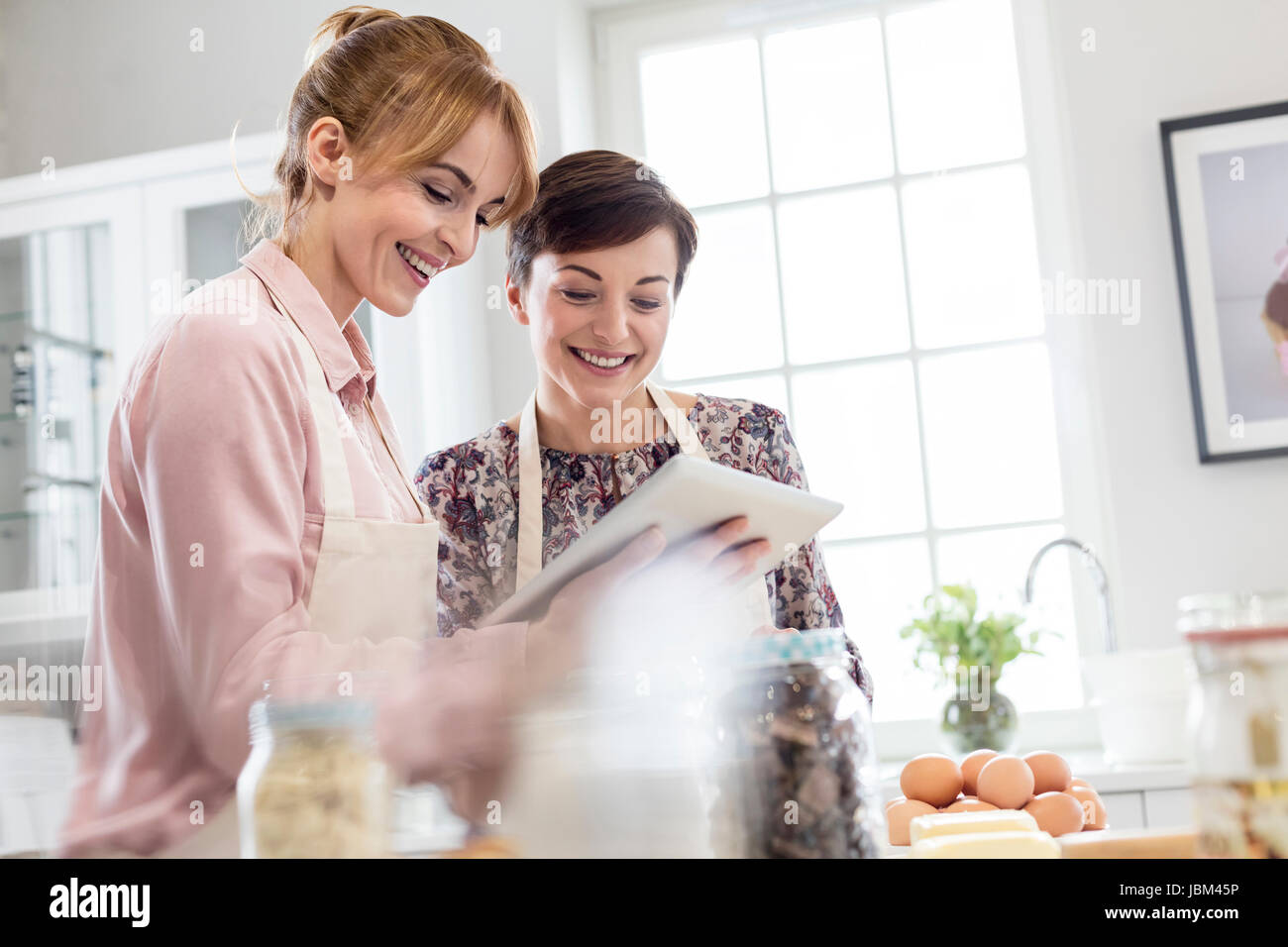 Smiling female caterers using digital tablet, baking in kitchen Stock Photo