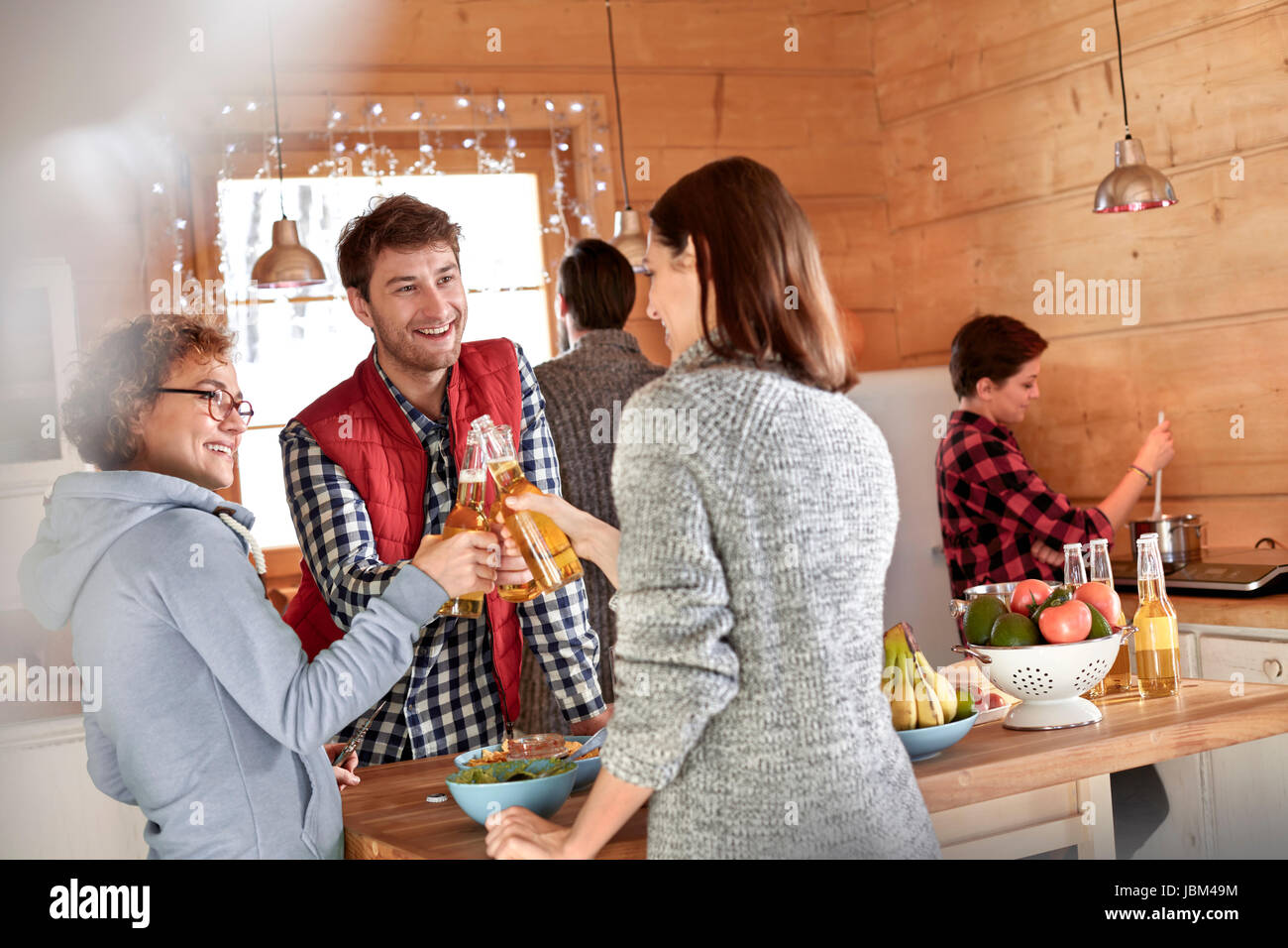 Friends toasting beer bottles in cabin kitchen Stock Photo