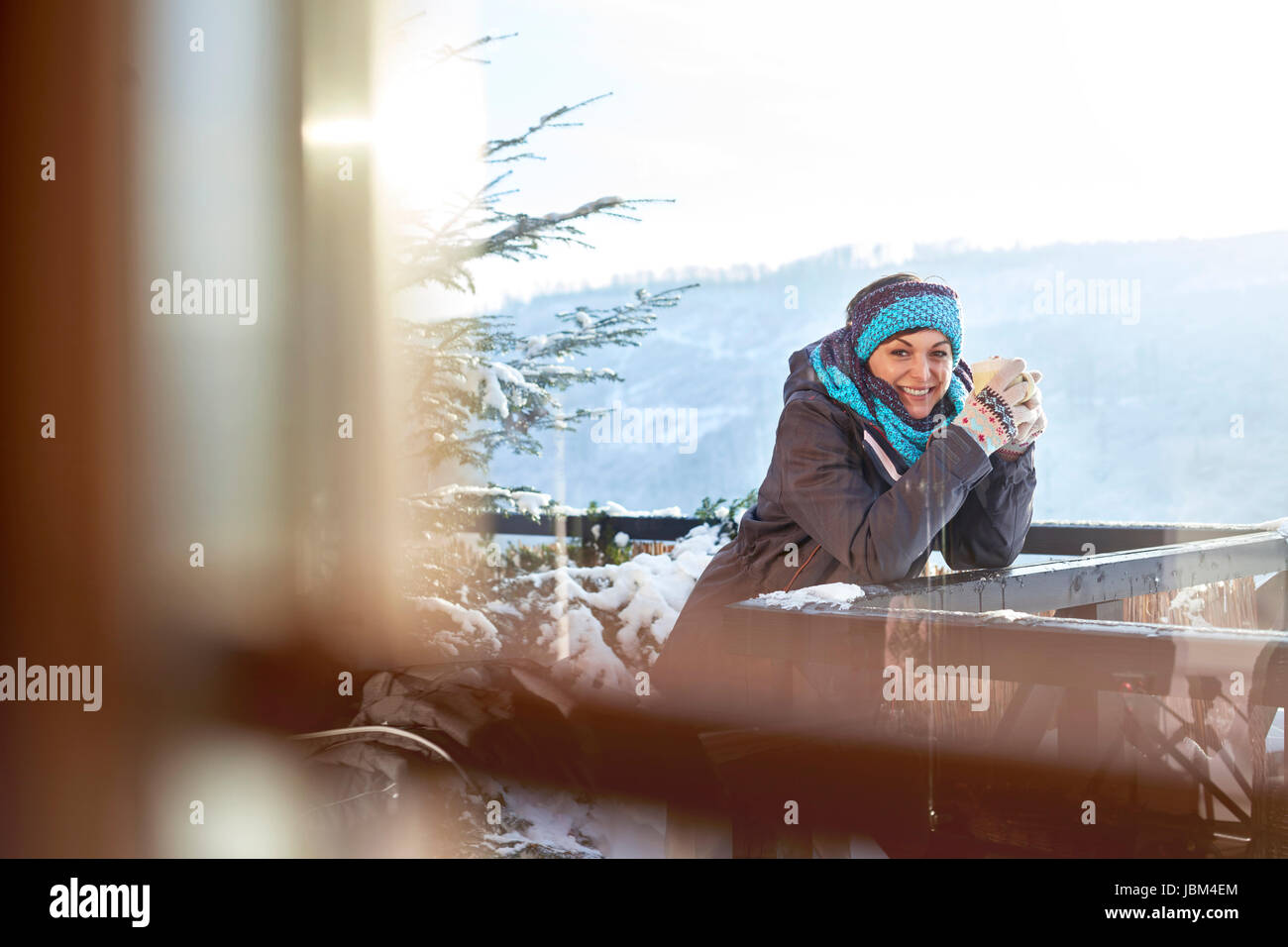 Portrait smiling female skier drinking hot cocoa on sunny cabin balcony Stock Photo