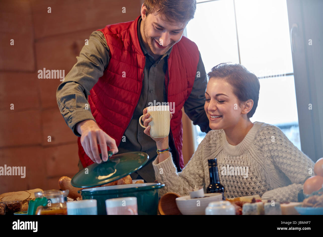 Couple cooking and drinking at cabin table Stock Photo