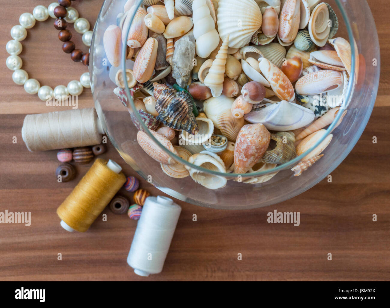Bowl of seashells with pearls, beads and thread nearby Stock Photo