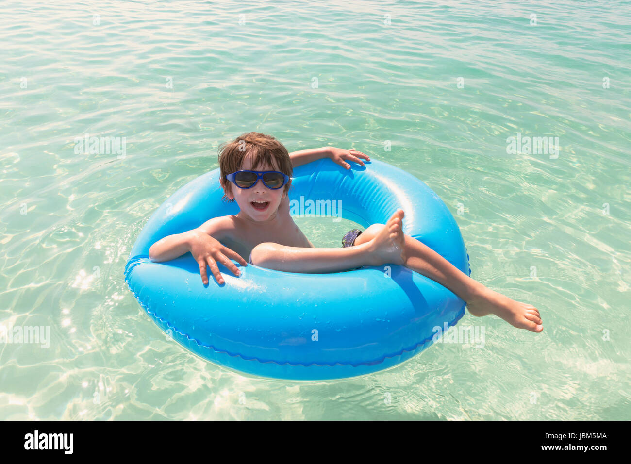 Portrait smiling boy in sunglasses floating in blue inflatable ring in ...