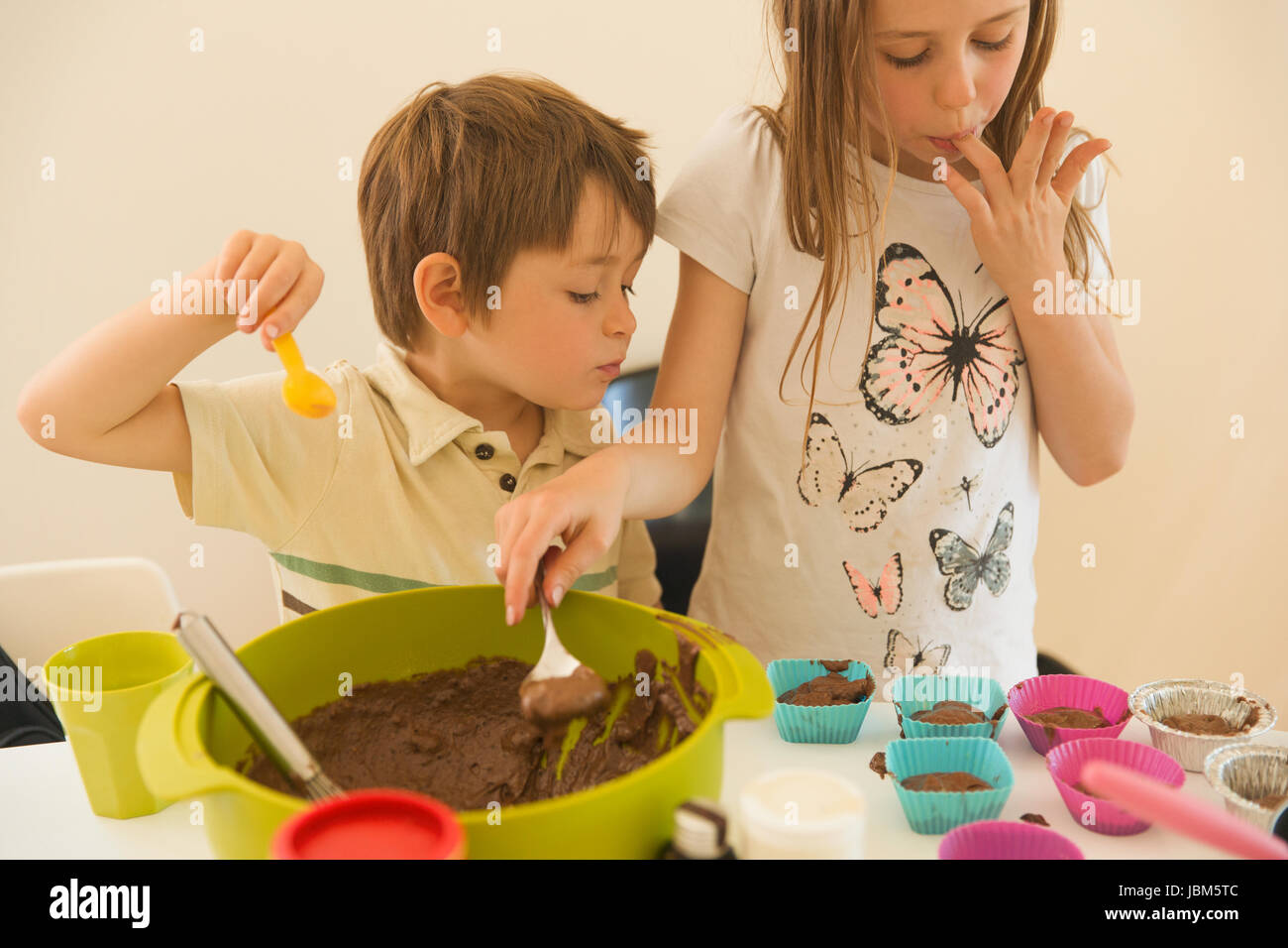 Boy and girl brother and sister making chocolate cupcakes, licking fingers Stock Photo