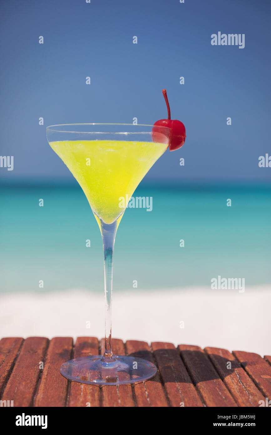 Yellow cocktail with cherry in martini glass on sunny tropical ocean beach Stock Photo