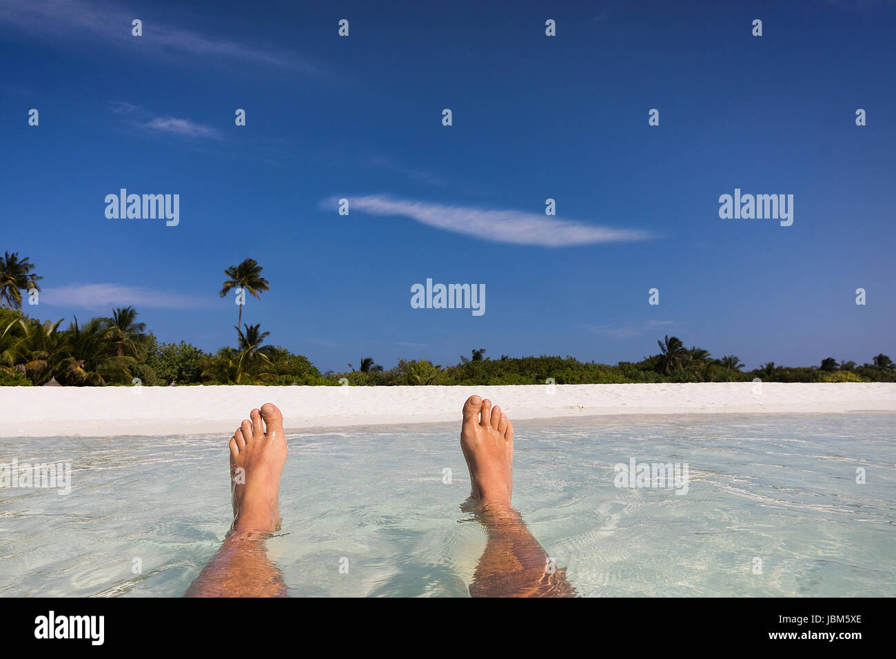 Personal perspective barefoot man floating in tropical ocean surf with view of beach Stock Photo