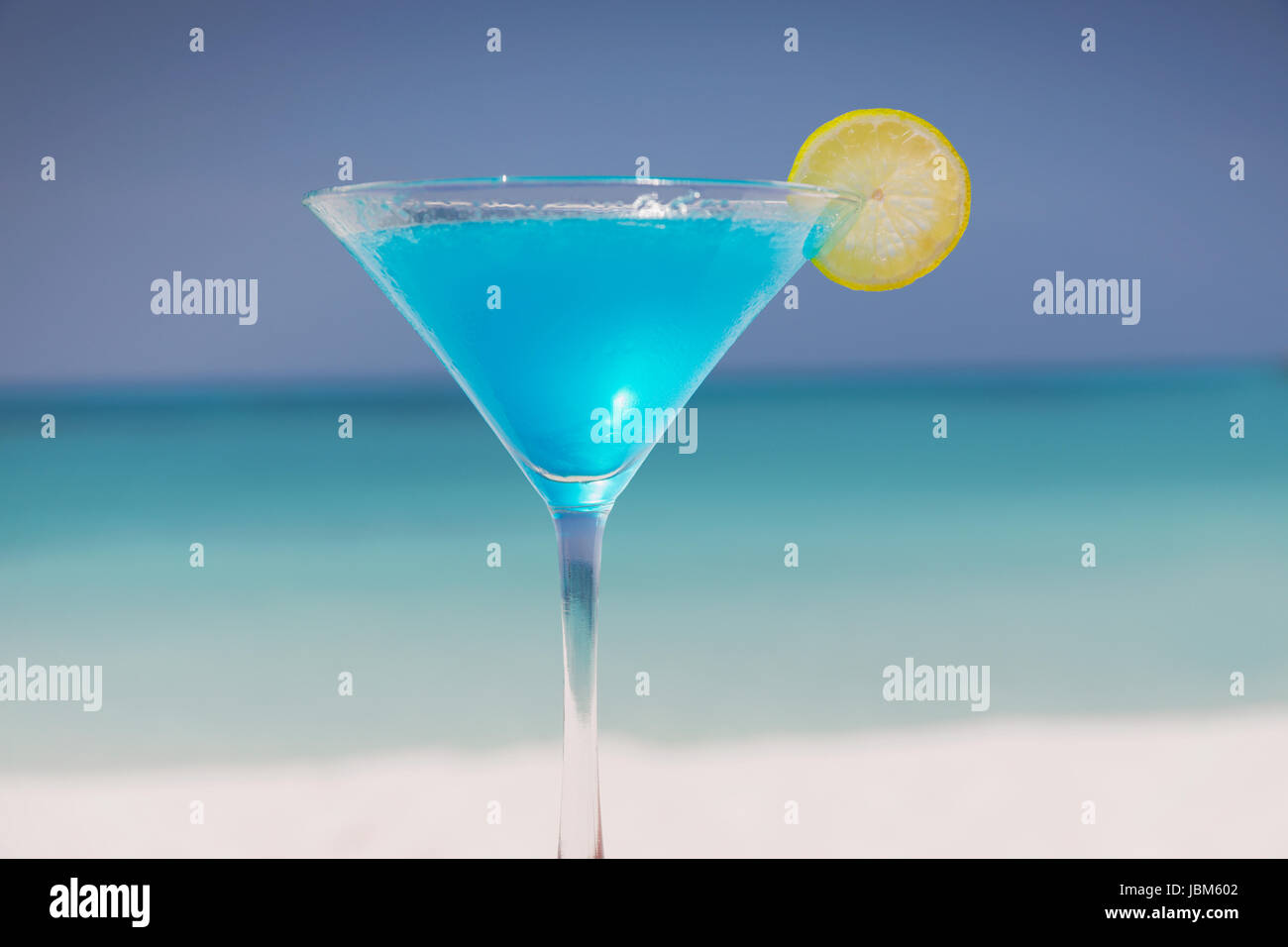 Blue cocktail with lemon slice in martini glass on tropical ocean beach Stock Photo