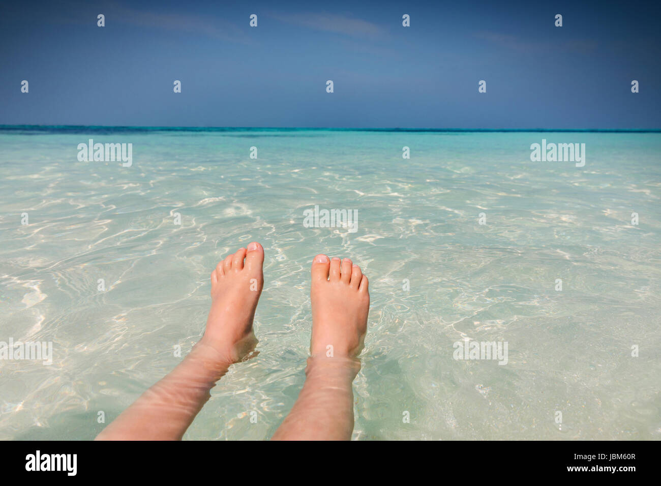 Personal perspective barefoot boy floating in tropical blue ocean Stock Photo