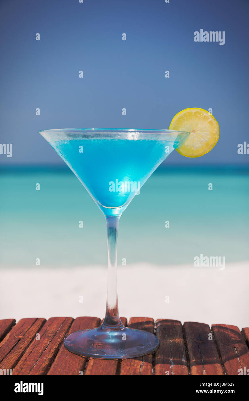 Blue cocktail with lemon slice in martini glass on sunny tropical beach Stock Photo
