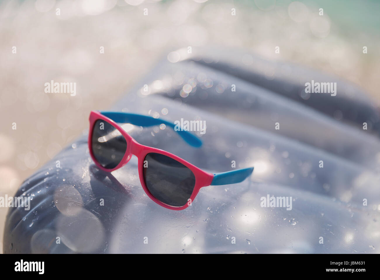 Close up pink and blue sunglasses on inflatable raft in sunny water ...