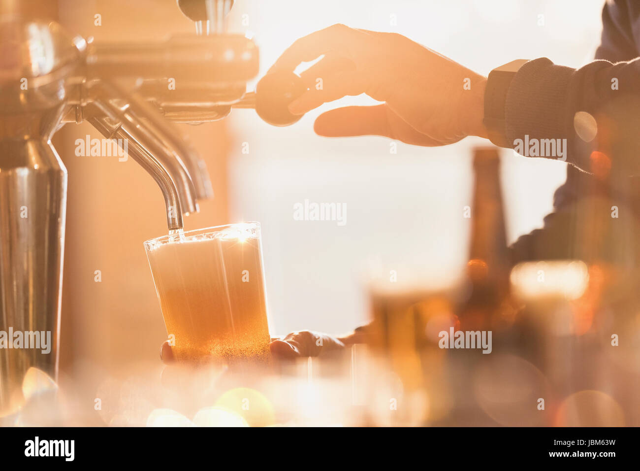 Close up male bartender pouring pint of beer from beer tap behind bar Stock Photo